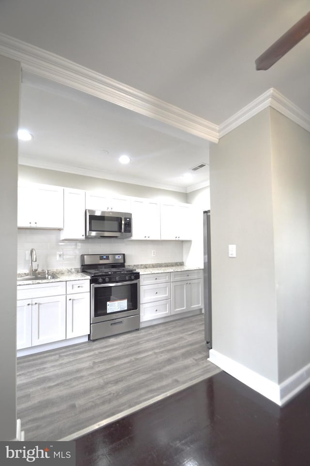 kitchen featuring baseboards, ornamental molding, wood finished floors, stainless steel appliances, and a sink