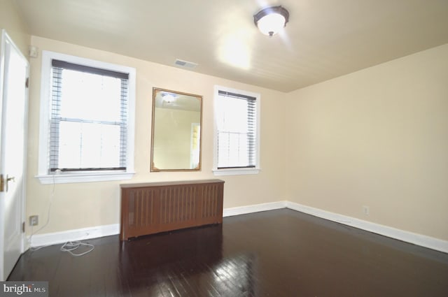 unfurnished room featuring visible vents, radiator, baseboards, and dark wood-style flooring