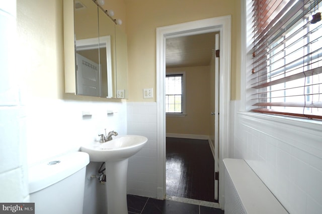 half bath with tile patterned floors, a wainscoted wall, toilet, and tile walls