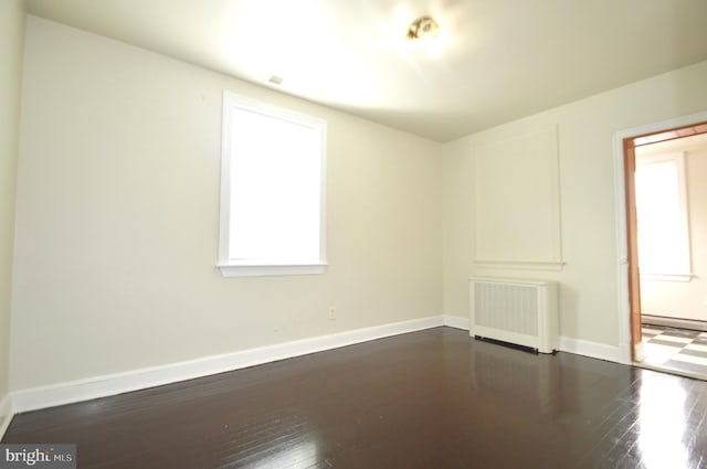 empty room featuring dark wood finished floors, radiator heating unit, and baseboards