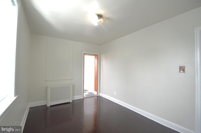 unfurnished room with baseboards, dark wood-style flooring, and radiator heating unit