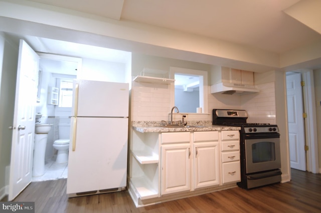 kitchen featuring a sink, under cabinet range hood, gas range, freestanding refrigerator, and open shelves