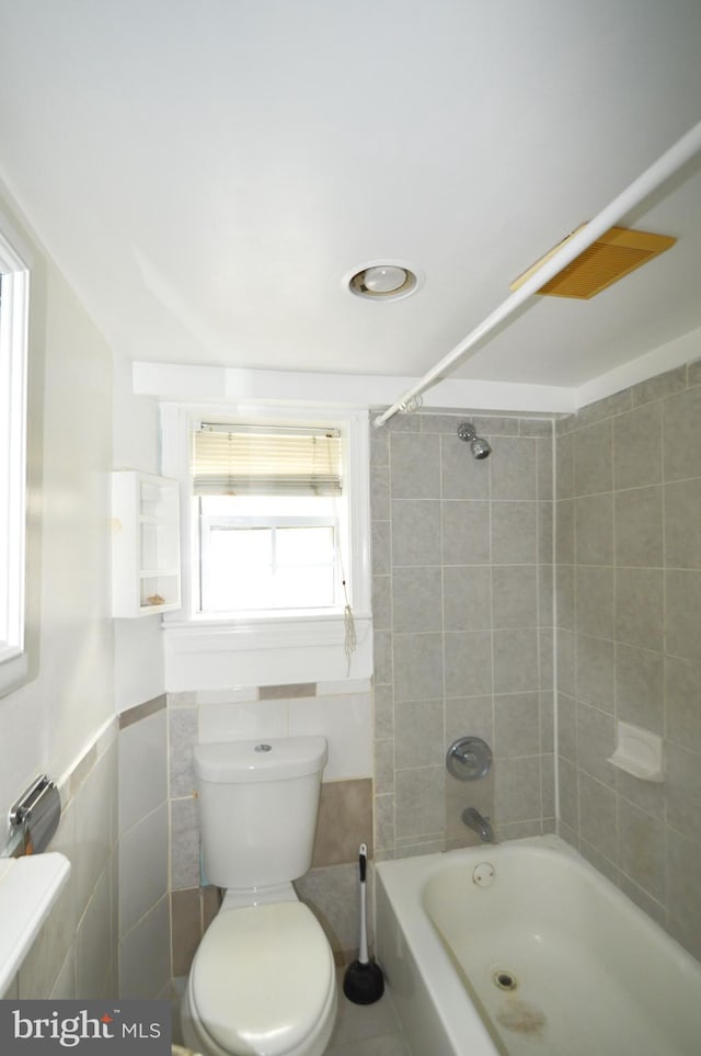 bathroom featuring toilet, tile walls, and shower / tub combination