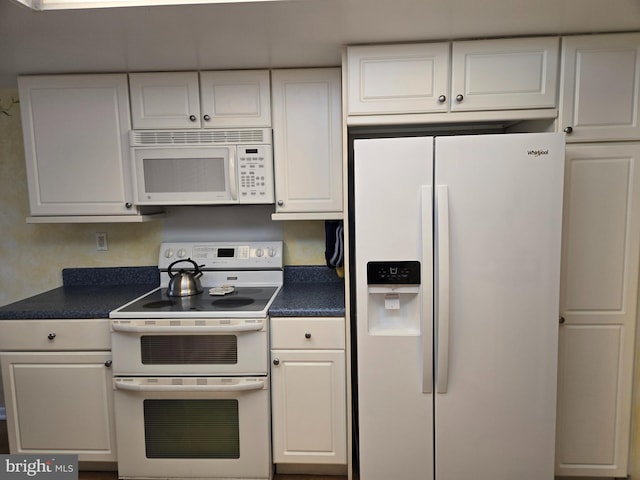 kitchen with white appliances, dark countertops, and white cabinetry