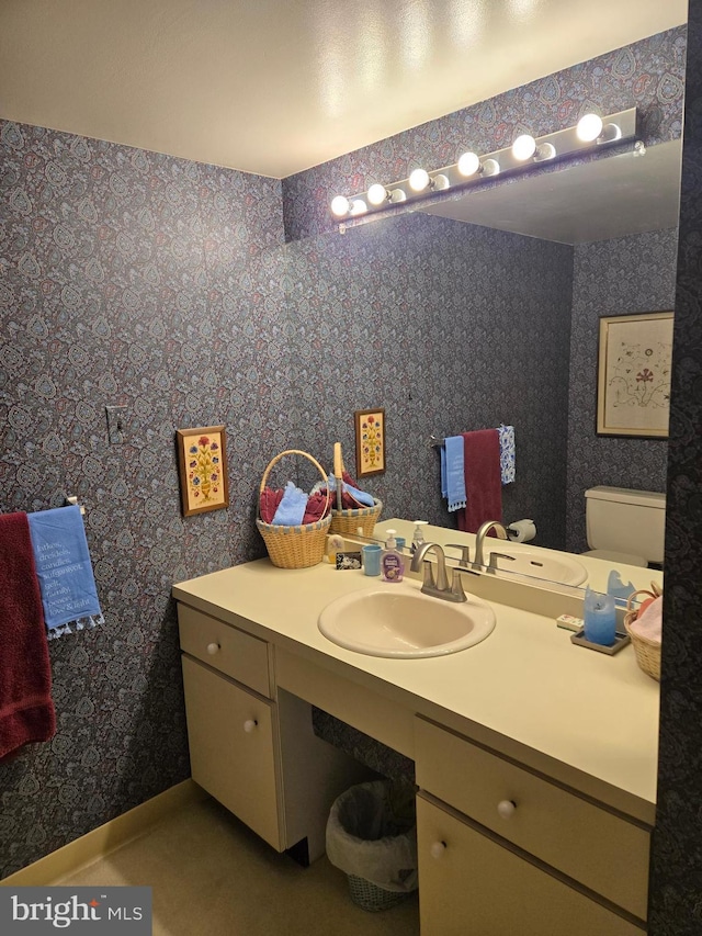 bathroom with toilet, wallpapered walls, vanity, and baseboards