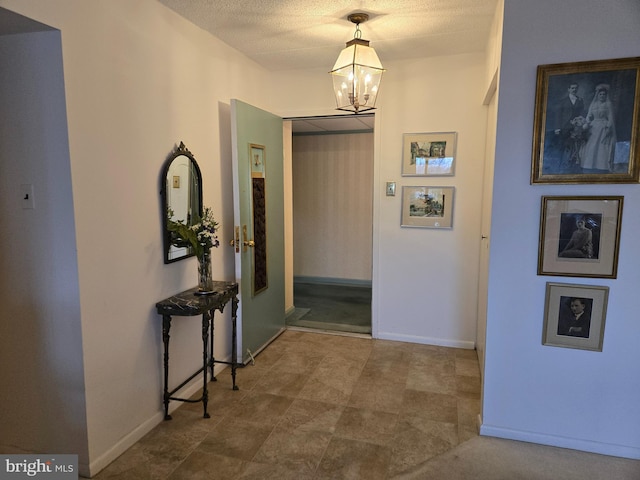 hallway featuring baseboards, a textured ceiling, and an inviting chandelier