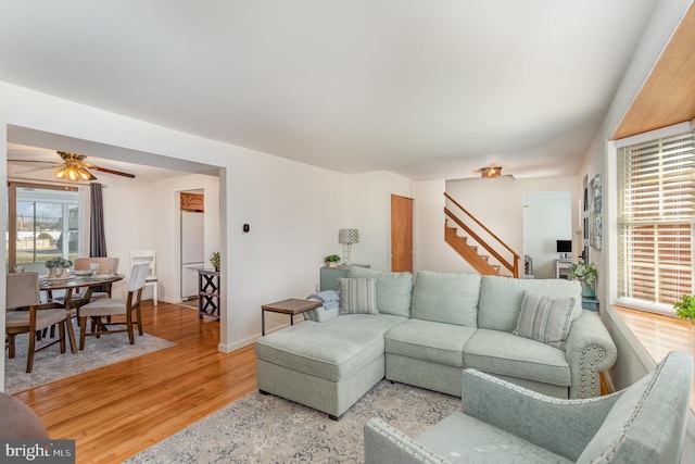 living area featuring baseboards, a ceiling fan, stairs, and light wood-style floors