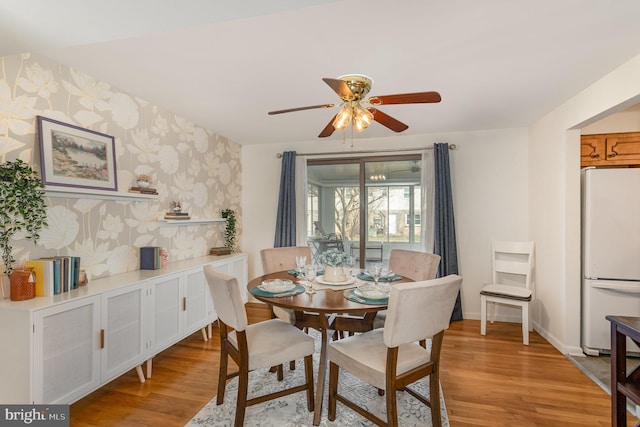 dining room featuring a ceiling fan, wallpapered walls, light wood finished floors, baseboards, and an accent wall