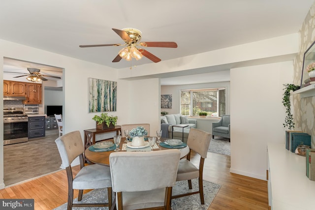 dining room featuring light wood-style flooring, a ceiling fan, and baseboards