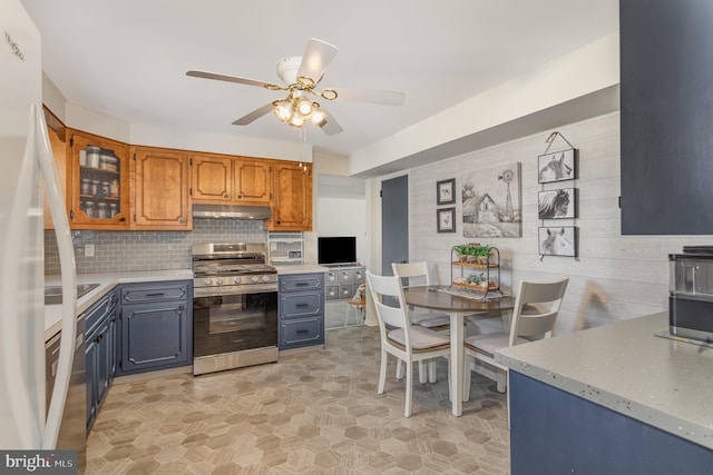 kitchen featuring brown cabinetry, stainless steel range with gas stovetop, ceiling fan, under cabinet range hood, and backsplash