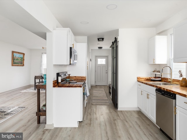 kitchen with light wood-style flooring, a sink, butcher block countertops, stainless steel appliances, and white cabinets