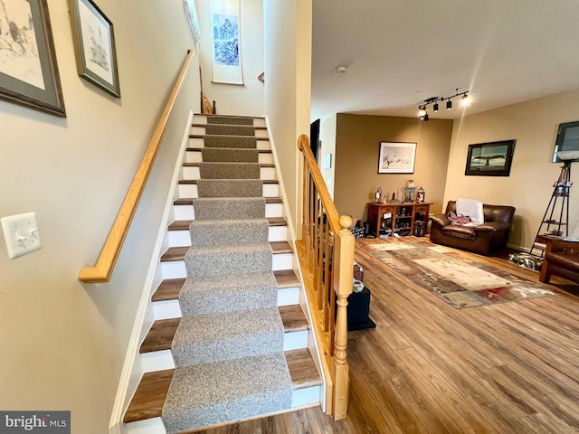 staircase with baseboards, wood finished floors, and track lighting