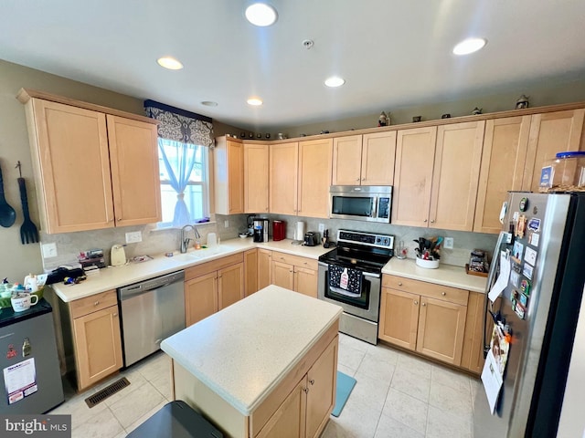 kitchen with light brown cabinetry, light countertops, decorative backsplash, appliances with stainless steel finishes, and a sink