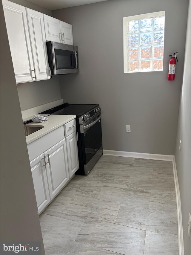 kitchen featuring electric stove, a sink, stainless steel microwave, white cabinetry, and baseboards