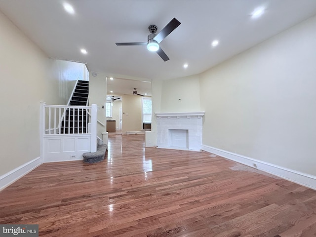 unfurnished living room featuring wood finished floors, stairway, a ceiling fan, and baseboards