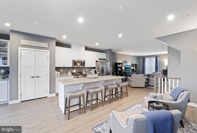 kitchen featuring a breakfast bar, a kitchen island with sink, appliances with stainless steel finishes, white cabinetry, and open floor plan