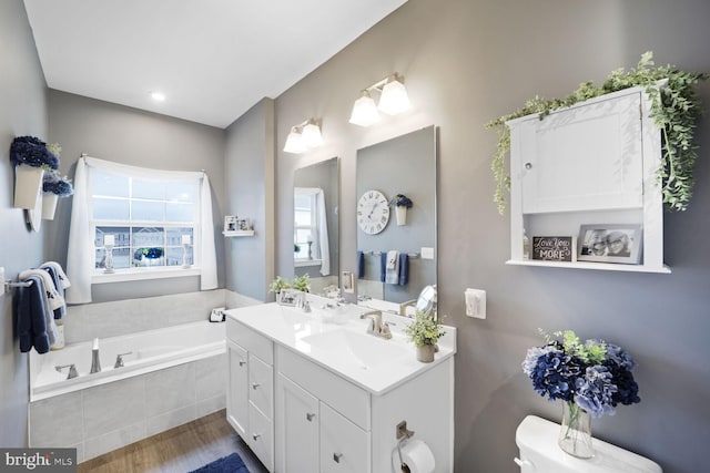 bathroom featuring wood finished floors, double vanity, a sink, a garden tub, and toilet