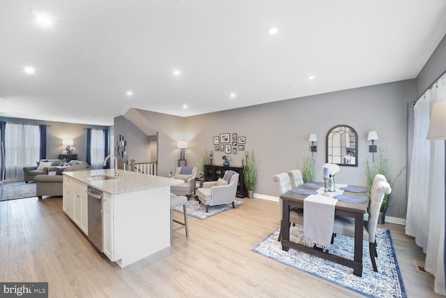 kitchen with open floor plan, light wood-type flooring, an island with sink, white cabinets, and a sink