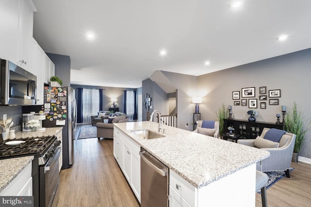 kitchen with a center island with sink, a sink, open floor plan, stainless steel appliances, and light wood-style floors