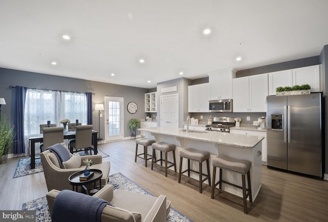 kitchen with a center island with sink, a sink, a kitchen breakfast bar, white cabinetry, and stainless steel appliances