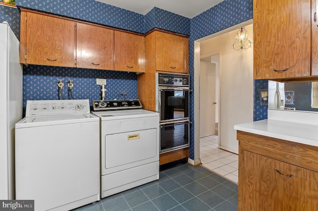 clothes washing area with baseboards, washing machine and clothes dryer, wallpapered walls, cabinet space, and dark tile patterned floors