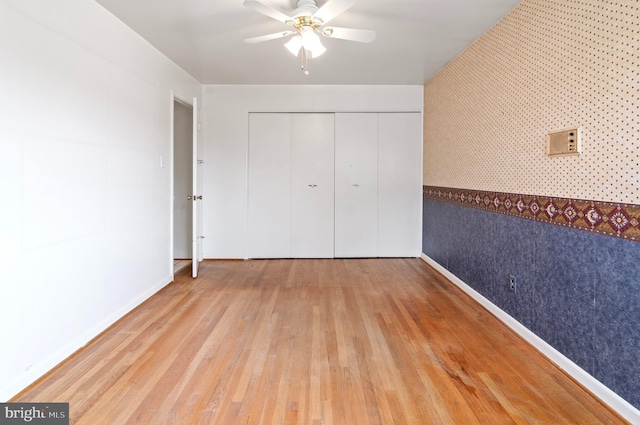 unfurnished bedroom featuring a closet, baseboards, wood finished floors, and wallpapered walls