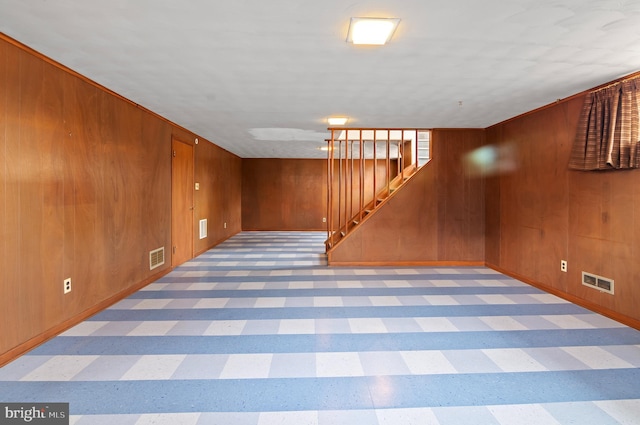 finished basement with visible vents, light floors, stairway, and wooden walls