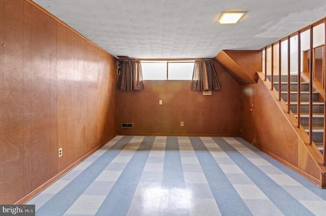 empty room with tile patterned floors, stairway, wood walls, and visible vents