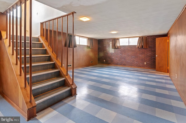 stairs with tile patterned floors, wood walls, and brick wall