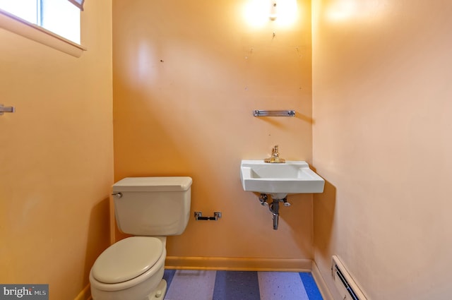 half bath featuring toilet, baseboards, baseboard heating, and a sink