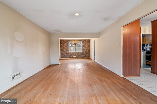 unfurnished room with a notable chandelier, light wood-type flooring, and baseboards