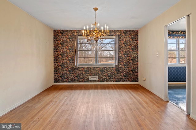 unfurnished dining area with wallpapered walls, wood finished floors, baseboards, and a chandelier