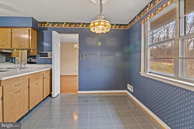 kitchen with baseboards, wallpapered walls, a sink, light countertops, and dark tile patterned floors