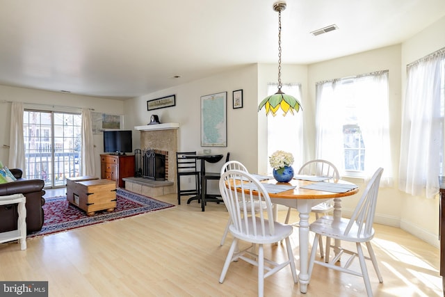 dining space featuring wood finished floors, a fireplace, visible vents, and baseboards