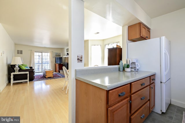 kitchen featuring brown cabinets, freestanding refrigerator, light countertops, light wood-style floors, and open floor plan