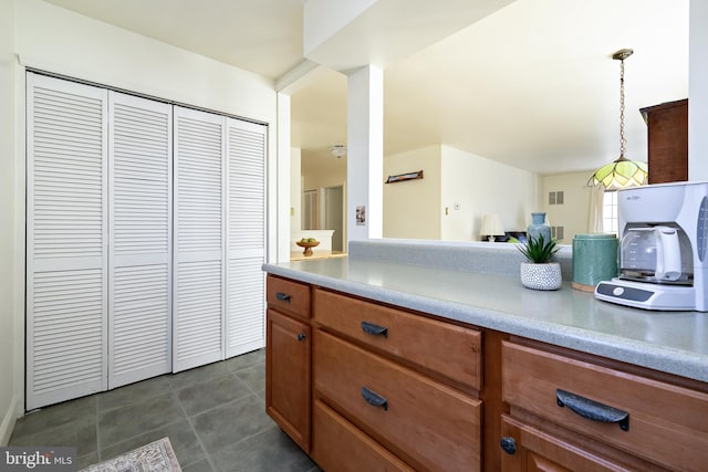 kitchen with brown cabinetry, visible vents, light countertops, pendant lighting, and dark tile patterned floors