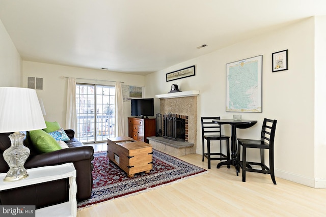 living area with a brick fireplace, wood finished floors, visible vents, and baseboards