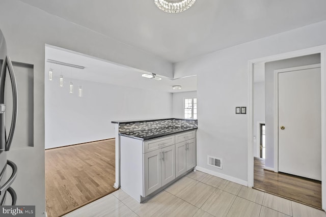 kitchen featuring visible vents, a peninsula, freestanding refrigerator, light wood-style floors, and dark countertops