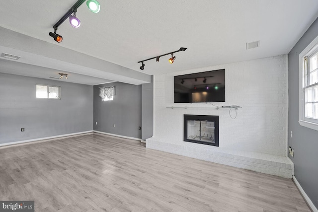 unfurnished living room featuring visible vents, baseboards, a fireplace, wood finished floors, and a textured ceiling