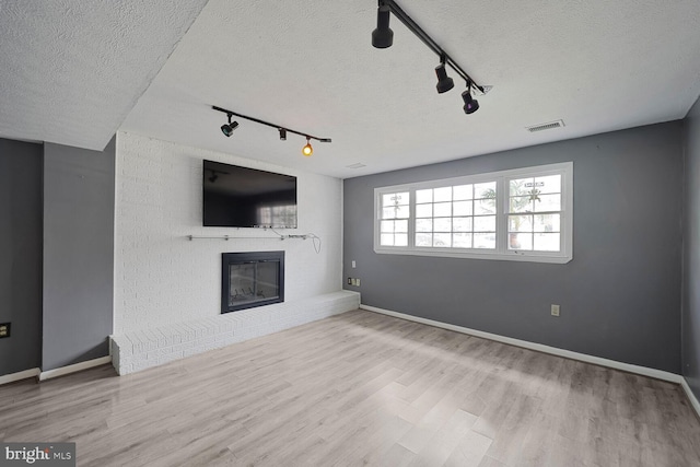 unfurnished living room featuring wood finished floors, baseboards, visible vents, a textured ceiling, and a brick fireplace