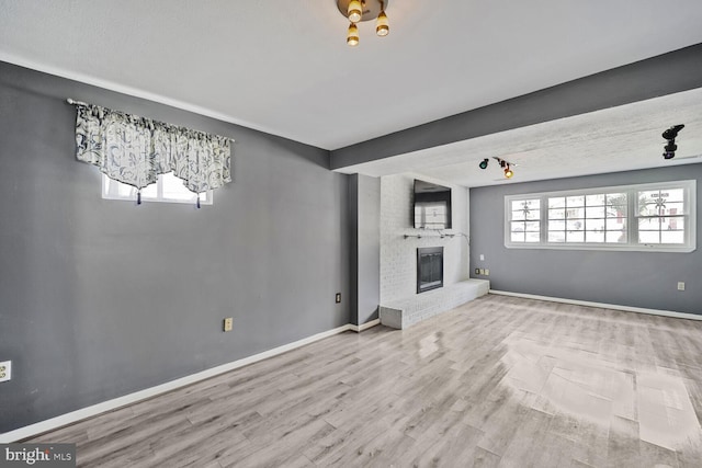 unfurnished living room with a brick fireplace, baseboards, and wood finished floors