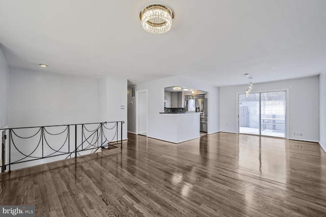 unfurnished living room featuring an inviting chandelier, wood finished floors, and visible vents