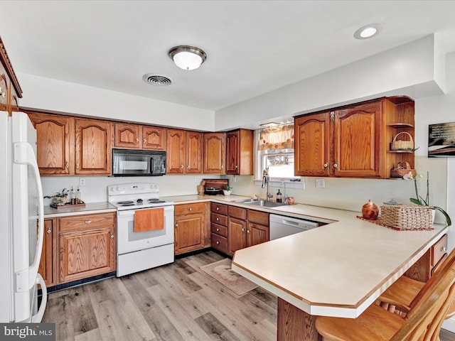 kitchen featuring visible vents, brown cabinets, a peninsula, white appliances, and a sink