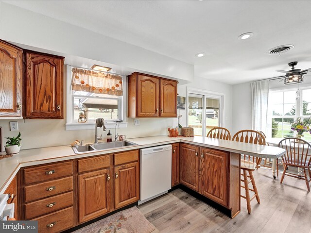 kitchen with visible vents, a peninsula, white dishwasher, brown cabinetry, and a sink