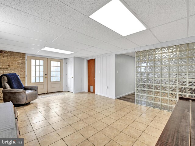 unfurnished living room featuring tile patterned floors, a drop ceiling, french doors, and baseboards