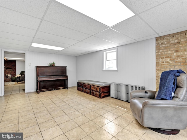 living area with light tile patterned floors, a drop ceiling, and radiator heating unit