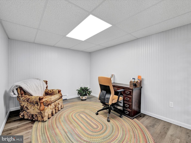 office area featuring a drop ceiling, baseboards, wood finished floors, and a baseboard heating unit