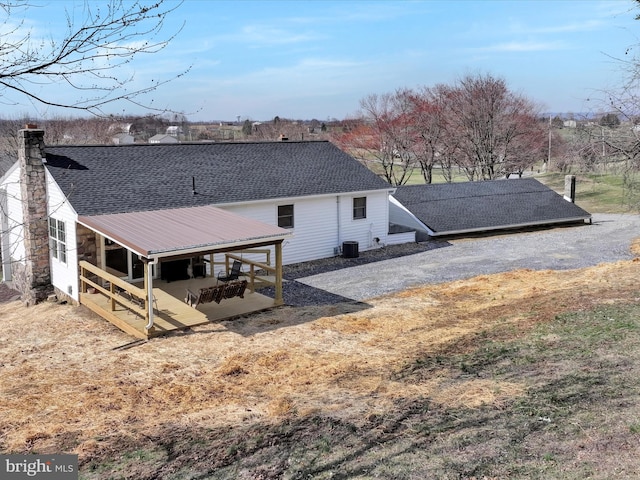 back of property with central AC unit and a shingled roof