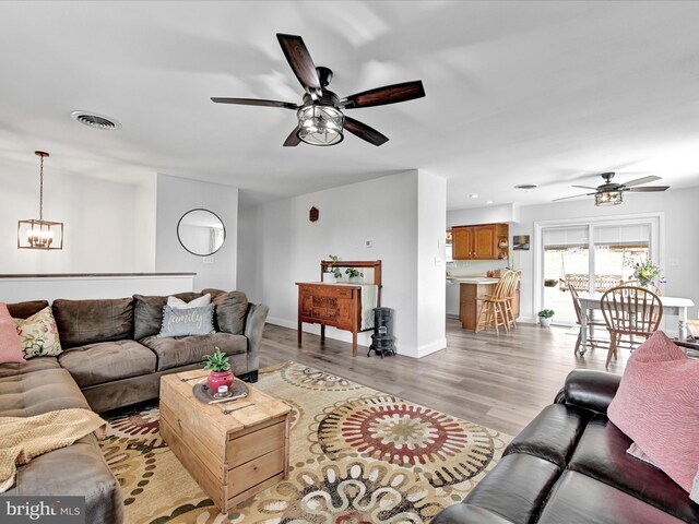 living area with light wood finished floors, visible vents, baseboards, ceiling fan with notable chandelier, and recessed lighting