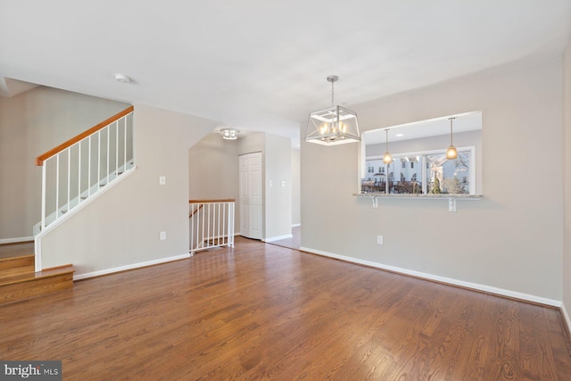 unfurnished living room featuring a notable chandelier, stairway, baseboards, and wood finished floors